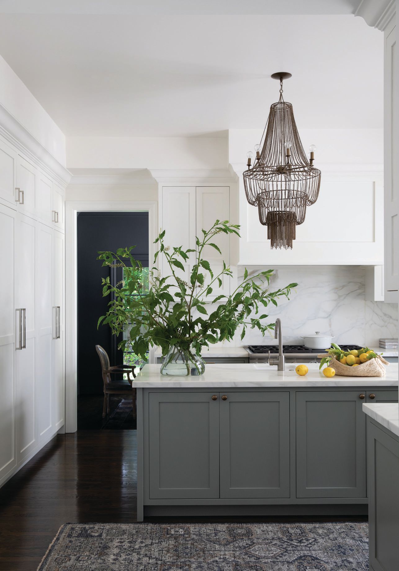 The kitchen shines with hardware from the Aspen Collection by Top Knobs, which is complemented by cabinets dressed with Benjamin Moore Simply White paint that contrasts the lower cabinets painted with Farrow & Ball’s Pigeon hue. The chandelier comes from Arteriors Home.  PHOTOGRAPHED BY BESS FRIDAY
